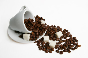Inverted white cup with coffee beans and sugar cubes dropped out