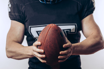 Muscular american football player in uniform and helmet holding ball, ready to play and fight for win, isolated over white background.
