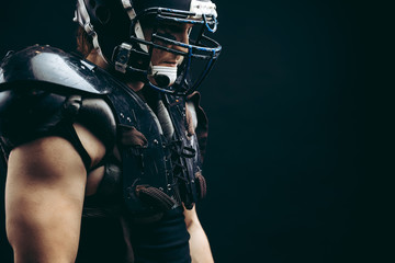 Head and shoulder portrait of muscular American football player wearing black helmet and protective...