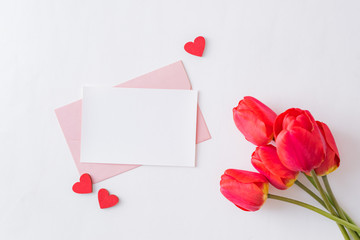 Mockup white greeting card, red  hearts and envelope with red tulips on a light  background