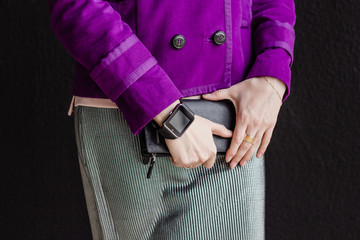 A woman holds a black leather clutch in her hands. On her wrist is a smart watch.