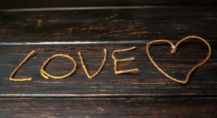 Fototapeta premium inscription love from a beautiful rope with a heart on a wooden background, valentines day