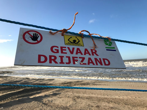 dutch sign at the beach warning for quick sand