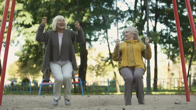 Two senior ladies enjoying ride on swings in park, elderly friends, retirement