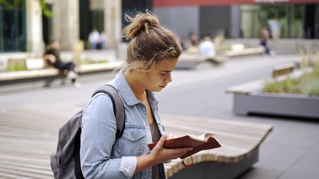 Side view of young female reading notes in notebook while standing on blurred background of student campus in Leipzig, Germany
