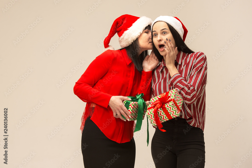 Poster Happy family in Christmas sweater posing with gifts. Enjoying love hugs, holidays people. Mom and doughter on a gray background in the studio