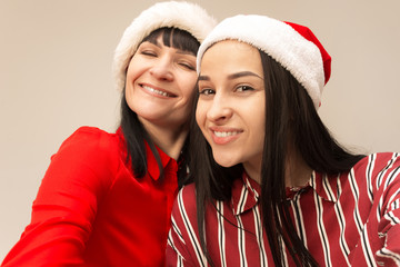 A portrait of a happy mother and daughter in Santa hat at studio on gray background. Human positive emotions and facial expressions concept