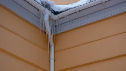 Icicles on the drainpipe and ditch. Incorrect installation of the drainage system, on which large icicles appear that pose a threat to the health and lives of people passing by.