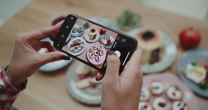 A women using her phone to take pictures of aesthetic foods on the table.