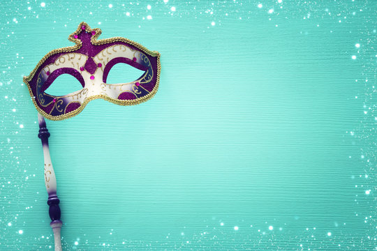carnival party celebration concept with elegant purple mask on stick over mint wooden background. Top view.