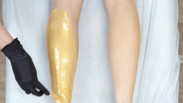 The beautician works with the paste and removes the hairs on the legs