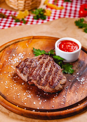 Grilled beef steak with tomato sauce on wooden cutting board. Close up