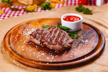 Grilled beef steak with tomato sauce on wooden cutting board. Close up