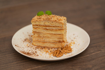 Piece of cake Napoleon on white plate on wooden background. Russian cuisine, layered cake with cream, close up view. Selective focus.