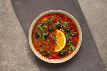 Soup with meat, olives, herbs, lemon in bowl, on grey  background, top view homemade food. Traditional Russian soup – solyanka