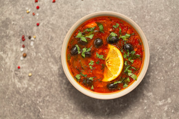Soup with meat, olives, herbs, lemon in bowl, on grey  background, top view homemade food. Traditional Russian soup – solyanka
