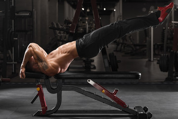 Muscular man working out in gym, doing exercise dragon flag for abs, strong male naked torso