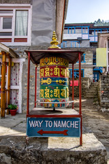 Fototapeta na wymiar Close up view of colorful prayer wheel. Pedestrian sign to Namche Bazaar. Sagarmatha (Everest) National Park, Nepal.