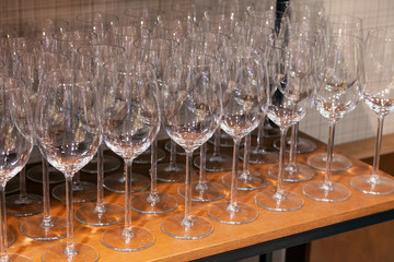 Many transparent crystal wine glasses stand in row on the brown wooden shelves of the rack. Side view. The concept of tasting whiskey, brandy, port on production in Scotland or Ireland