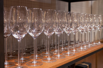 Many transparent crystal wine glasses stand in row on the brown wooden shelves of the rack. Side view. The concept of tasting whiskey, brandy, port on production in Scotland or Ireland