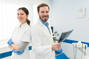 Fototapeta premium Portrait of two young attractive female and male doctor looking at camera holding a x-ray screening working in modern clinic. Successful young doctors concept.