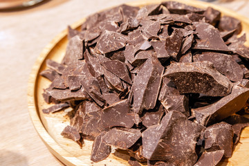 Close-up of a pile of pieces of natural dark chocolate on a round wooden plate. Concept diet, healthy food, lowcalorie dessert, carob