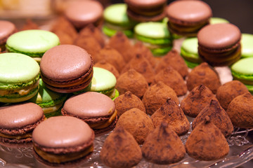 Closeup chocolate and pistachio macaroons and truffles sprinkled with cocoa in a crystal plate. View from above. Concept table birthday desserts, bakery degustation