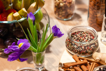 Closeup snacks, purple irises, fresh and dried fruits, red, white and black pepper mix in glass bowl, cinnamon sticks, nuts. Concept degustation premium alcohol at opening of shoes store