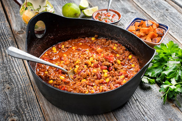 Traditional slow cooked Mexican chili con cane with mincemeat, beans and corn as closeup in a modern design cast-iron roasting dish - obrazy, fototapety, plakaty