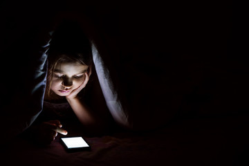 The girl under a blanket with a smartphone.