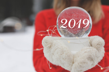 Woman in warm knitted mittens holding snow globe and Christmas lights outdoors, space for text....