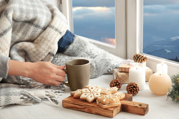 Woman relaxing with cup of hot winter drink near window. Cozy season