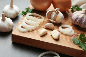 Wooden board with garlic and onion rings on table, closeup