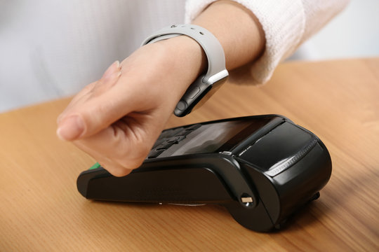 Woman using terminal for contactless payment with smart watch at table, closeup