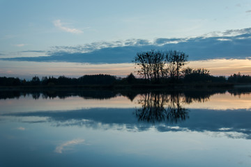 Gray cloud and trees on the shore reflecting in the lake