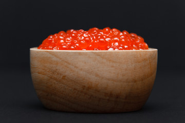 Closeup macro saucer or bowl with slide of fresh tasty red salmon caviar on black background. Side view. Concept gourmet snack seafood appetizer