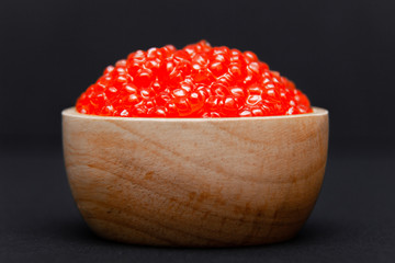 Closeup macro saucer or bowl with slide of fresh tasty red salmon caviar on black background. Side view. Concept gourmet snack seafood appetizer