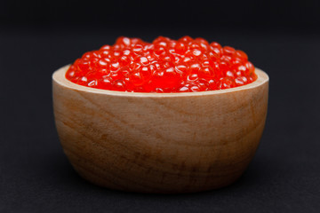 Closeup macro saucer or bowl with slide of fresh tasty red salmon caviar on black background. Side view. Concept gourmet snack seafood appetizer