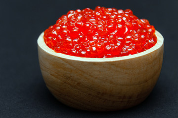 Closeup macro saucer or bowl with slide of fresh tasty red salmon caviar on black background. Top view. Concept gourmet snack seafood appetizer
