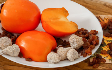 Delicious fresh persimmon fruit , raisins and dried figs  on the plate  and wooden table