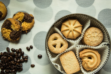 Cookies in a round box and coffee beans on a tablecloth with polka dots