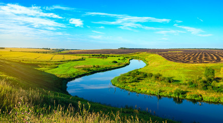 Sunny summer landscape with river bend,fields,green hills and beautiful clouds in blue sky at sunrise.