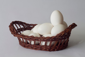 white chicken eggs in a wicker old basket on a white background