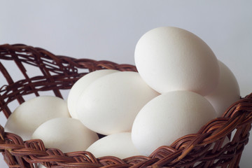 white chicken eggs in a wicker old basket on a white background