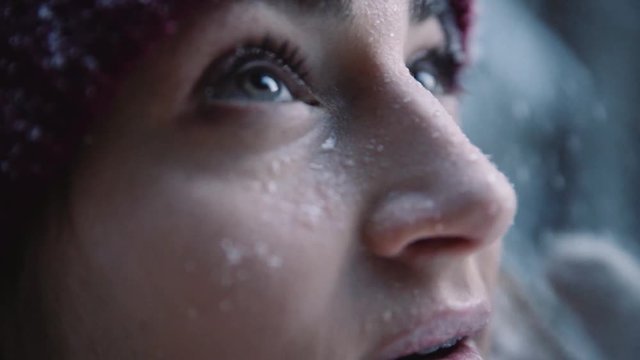 Beautiful eyes young woman in hat snow falls on face looking up in winter park cold girl happy nature white holiday outdoor pretty attractive fashion fun happiness model portrait slow motion