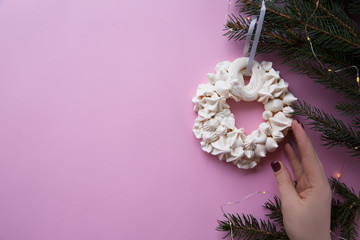 Christmas meringue wreath with hand on the fir branch on the pink color background. Flat lay