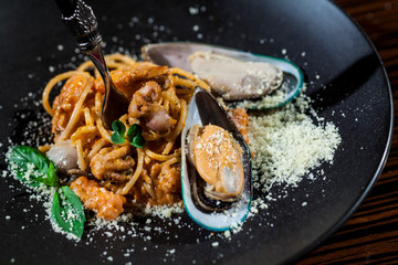 pasta with seafood and mussels and parmesan on a black plate