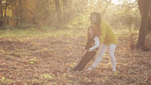 Happy young mother and her little redhead daughter having Fun in an autumn park. They playing and laughing. Slow motion