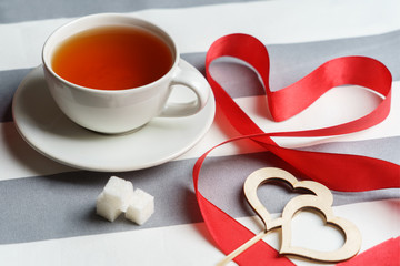 Romantic still life with a cup of tea and bright red holiday attributes.