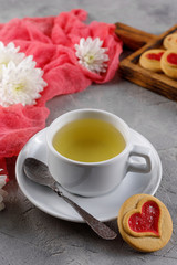 Cup with green tea and cookies with a heart on a decorative board is an ornament from fresh flowers. Valentine's day concept.